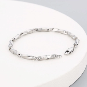 Détail d'un bracelet Mobius en acier au titane argenté avec fermoir mousqueton sur socle blanc