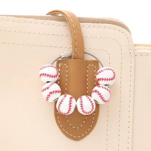 Baseball monogram charm with seven mini white balls on a beige leather handbag