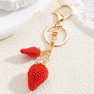 Detalle de llavero con colgante de fresa roja y herrajes dorados sobre base de piedra