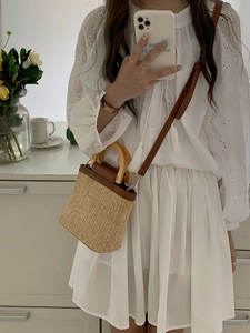Close-up of woven straw bucket bag with wood handle and brown leather trim detailing