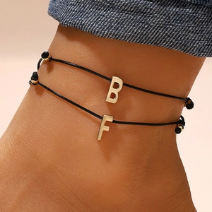 Close-up of black string anklets featuring gold initial B and F charms on the ankle