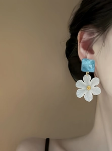 Close-up of elegant white acrylic flower earrings with blue marble stud on model