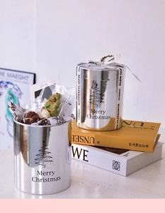 Close-up of a silver Christmas gift tin featuring minimalist tree and festive lettering