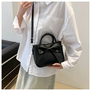 Close-up of a black crossbody bag with large bow detail and gold-tone hardware