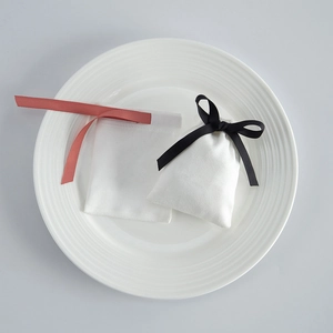 Macro shot of white velvet jewelry drawstring pouches with red and black ribbons on a tray