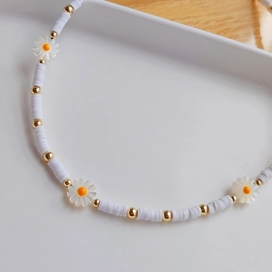 Macro detail of white heishi bead necklace featuring small daisy charms and gold spacer beads