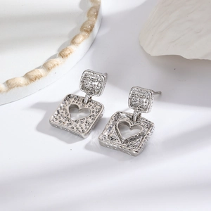 Macro detail of silver square earrings featuring a hollow heart pattern and textured surface
