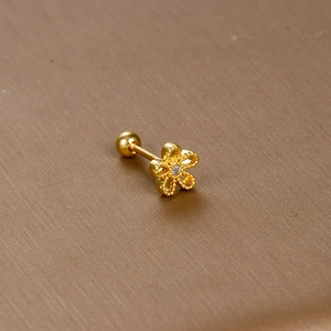 Macro shot of gold floral tragus stud with zircon center on a textured background