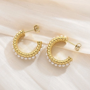 Detailed shot of golden C-shaped twisted earrings with white pearls on silk fabric