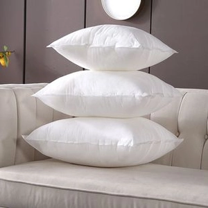 Detail view of premium white embroidered cushion covers stacked on a beige fabric sofa