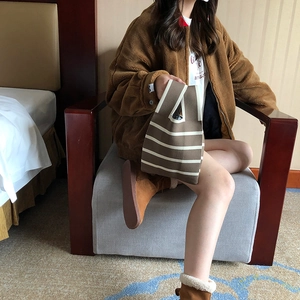 Detail of a brown and beige striped knitted tote bag held by a model on a sofa
