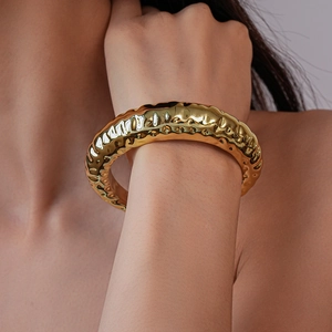 Detailed view of chunky golden cuff bracelet featuring a unique hammered metal texture