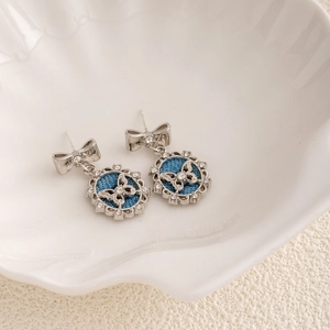 Macro detail of silver bow earrings with butterfly pattern on blue denim in a shell tray