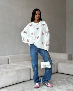 Detail of white round neck knit sweater with red hand-painted heart patterns and soft texture