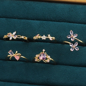 Détail de cinq bagues dorées avec gemmes roses papillon et fleurs sur velours vert