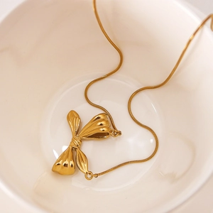 Elegant gold bow pendant necklace with sleek snake chain in a white ceramic dish