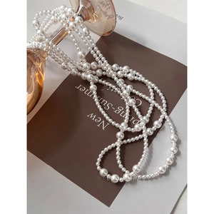 Detail view of long pearl necklace with various sized beads draped over a glass