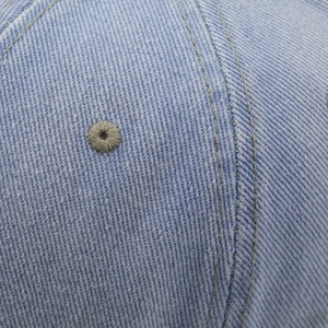 Dettaglio macro dell'occhiello traspirante e delle cuciture rinforzate sul berretto denim blu