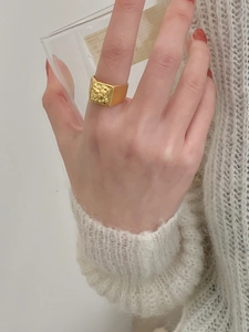 Macro detail of a vintage gold square embossed ring styled on a white knit sweater