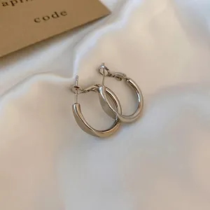 Minimalist silver-colored twisted hoop earrings with a sleek metallic finish on white silk