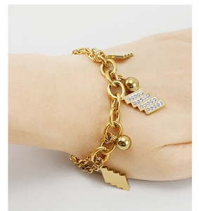 Dettaglio di un bracciale in acciaio dorato con pendenti geometrici e diamanti incastonati