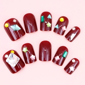 Detailed view of deep red press-on nails with colorful rhinestones on pink background