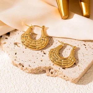 Macro shot of gold-plated thick U-shaped hoop earrings with textured quilted finish on stone