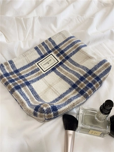 Macro view of plaid woolen toiletry bag showing soft fabric texture and stitched logo