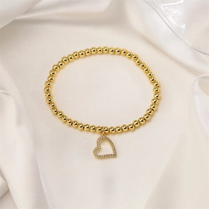 Detail of gold beaded bracelet with a hollow heart charm on elegant white silk cloth