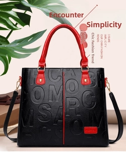 Close-up of black lychee grain leather tote bag with red handles and gold hardware