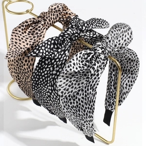 Three stylish leopard print bow headbands in beige, black, and grey on a gold stand
