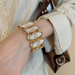Detail view of retro gold bracelet with white enamel oval panels on model's wrist