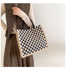Detail of checkered linen tote bag with black strap worn over the shoulder for commute