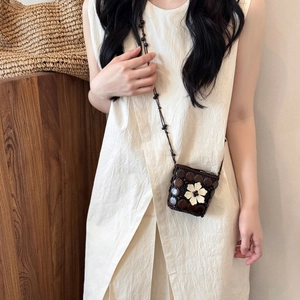 Detail of bohemian coconut shell crossbody bag with white flower and woven texture