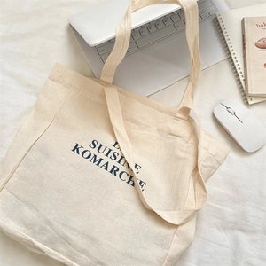 Detailed view of canvas tote bag with blue letter print on a minimalist desktop setting