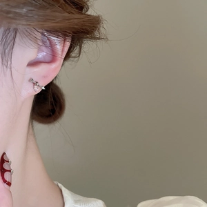 Close-up of a silver arrow stud earring with pink heart crystal worn on the earlobe