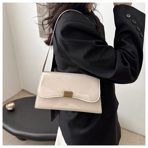 Detail of a chic cream-colored patent leather baguette bag with a golden buckle accent
