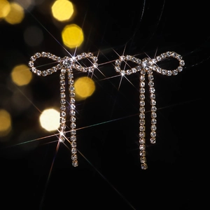 Sparkling bow tassel earrings with crystals on a deep black background with bokeh