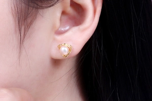 Macro shot of pale pink freshwater pearl earring with golden triangle frame on ear