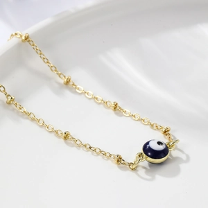 Macro shot of gold evil eye bracelet featuring blue enamel bead and fine chain detail