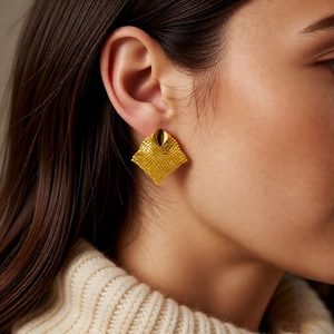 Detailed view of model wearing gold geometric mesh fringe earrings with woven metal texture