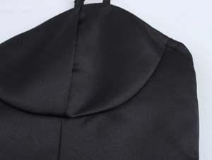 Detail of elegant black silk strap dress showing smooth texture and neckline stitching