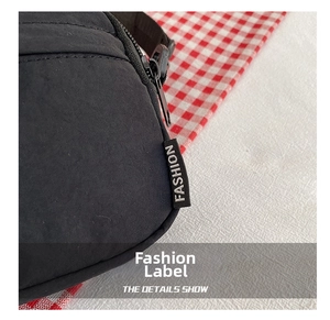 Close-up of the fashion label and zipper on the black nylon crossbody bag side