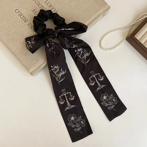 Detailed close-up of a black satin bow scrunchie with white linear floral prints