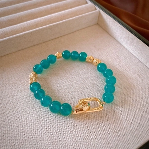 Detail of beaded necklace with teal stones and textured gold links on beige tray