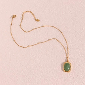 Golden necklace with oval green stone pendant and beads on a soft pink background
