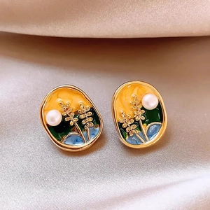 Macro detail of enamel flower earrings with pearls and gold floral patterns on silk