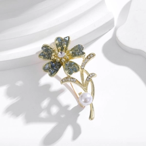 Detail of floral brooch featuring green crystal petals and a white pearl on a golden finish