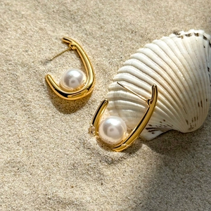 Gros plan de boucles d'oreilles en U dorées 18k avec perle blanche sur le sable