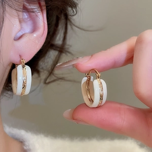 Close-up of vintage gold hoop earrings with white enamel finish on a model's ear